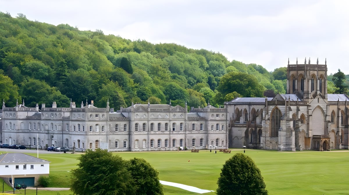 Das historische Hauptgebäude der Milton Abbey School ist von grünen Rasenflächen und Bäumen umgeben.