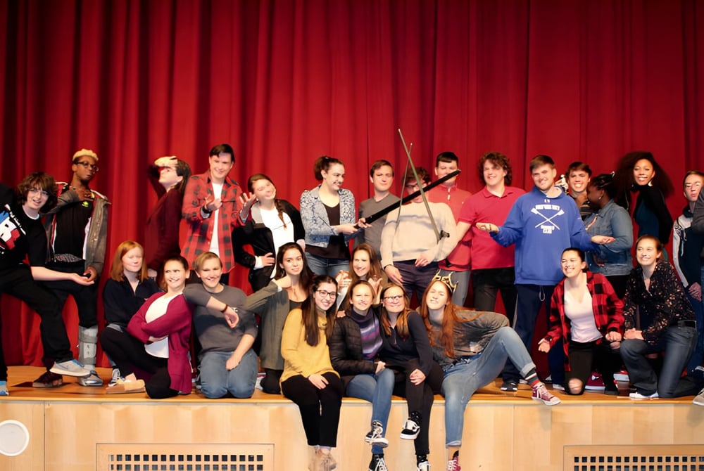 Eine Gruppe von Schülerinnen und Schülern der Milton District High School steht gemeinsam auf einer Bühne vor einem roten Vorhang.