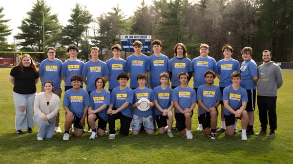 Eine Gruppe Schülerinnen und Schüler der Milton District High School posiert gemeinsam auf einem Rasenfeld mit Kiefern im Hintergrund.