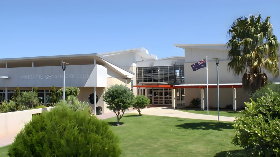 Das moderne weiße Gebäude mit Palmen und gepflegtem Rasen auf dem Campus des Mindarie Senior College vor klarem blauem Himmel.