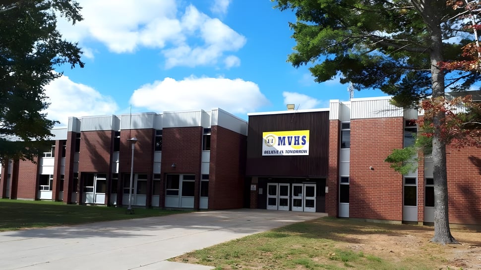 Das Backsteingebäude der Miramichi Valley High School ist umgeben von Bäumen und einer Rasenfläche unter blauem Himmel.