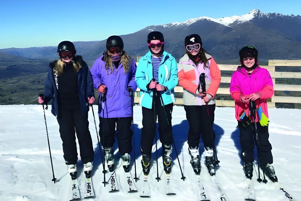 Eine Gruppe von Schülern der Miramichi Valley High School steht in bunter Winterkleidung auf einem schneebedeckten Berghang mit schneebedecktem Gipfel im Hintergrund.