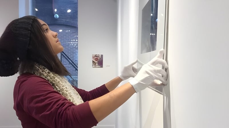 Eine Person in einem weinroten Pullover reinigt ein Fenster auf dem Campus der Miss Hall’s School vor einer Backsteinwand.