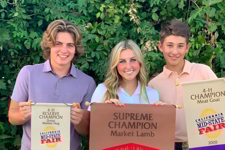 Drei Schüler der Mission College Preparatory Catholic High School präsentieren ihre gewonnenen Auszeichnungen vor einer grünen Umgebung.