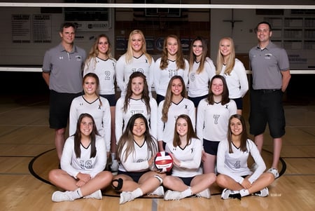 Eine Gruppe weiblicher Volleyballspielerinnen der Mission Secondary School posiert auf dem Basketballfeld vor der Anzeigetafel.