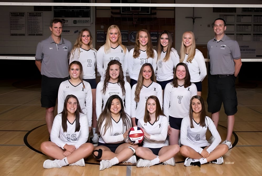 Eine Gruppe weiblicher Volleyballspielerinnen der Mission Secondary School posiert auf dem Basketballfeld vor der Anzeigetafel.