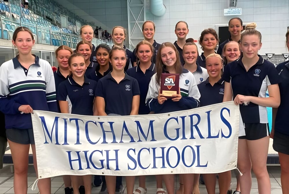 Eine Gruppe Schülerinnen der Mitcham Girls High School hält ein Banner in einer Sporthalle.