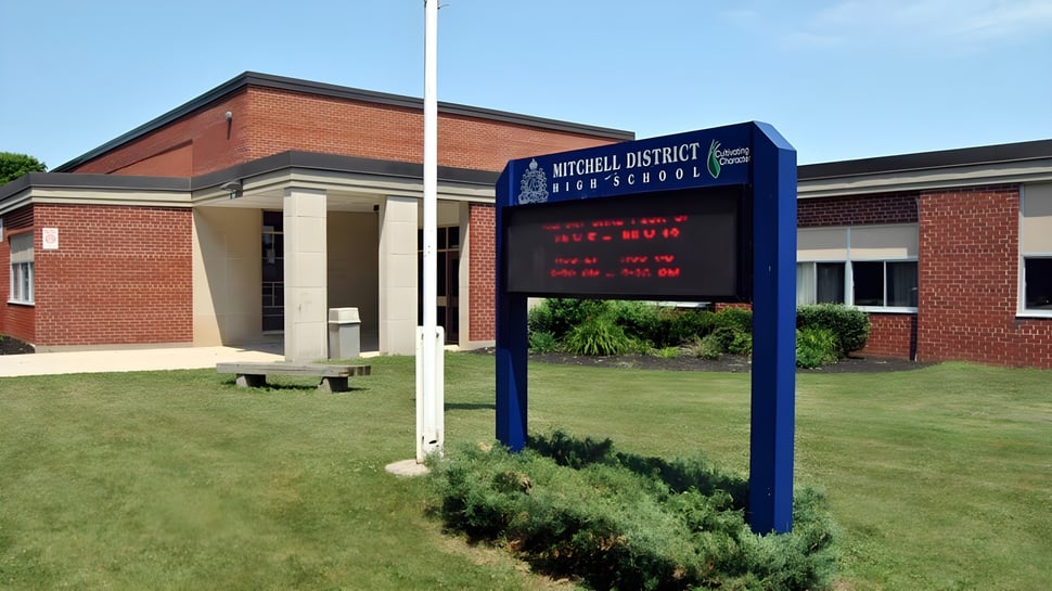 Das Backsteingebäude mit digitalem Anzeigeschild vor der Mitchell District High School ist von einer gepflegten Grünfläche umgeben.
