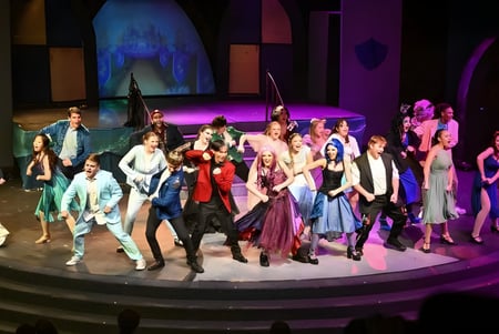 Eine Gruppe von Schülerinnen und Schülern in bunten Kostümen steht auf der Bühne der M.M. Robinson High School vor einem abstrakten Hintergrund.