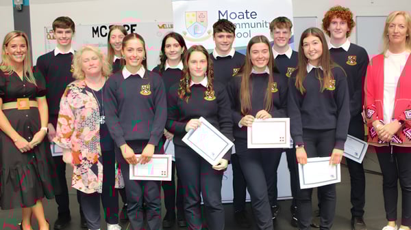 Schüler in Schuluniformen stehen mit Urkunden vor dem Eingang des Moate Community College.
