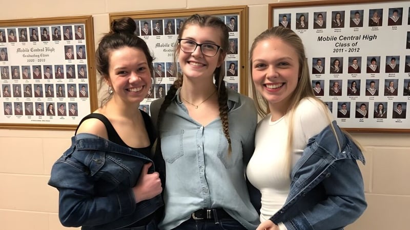 Drei Schuelerinnen stehen gemeinsam vor einer Wand mit Klassenfotos an der Mobile Central High.