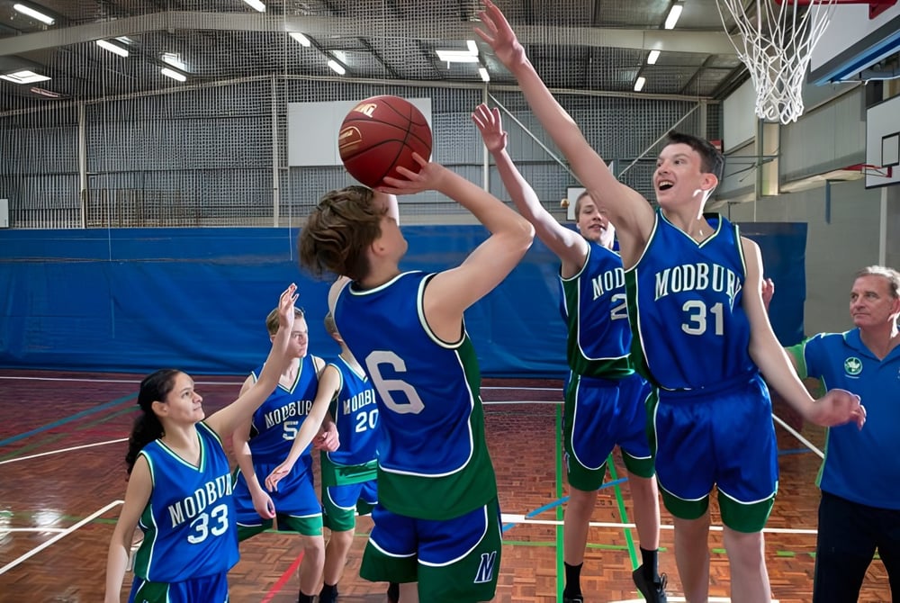 Eine Gruppe von Basketballspielern der Modbury High School konkurriert auf dem Spielfeld, während ein Spieler einen Wurf blockiert.
