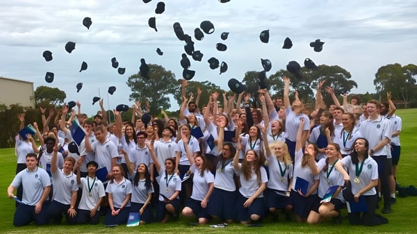 Eine Gruppe Schüler der Modbury High School wirft im Freien ihre Mützen hoch zur Feier.