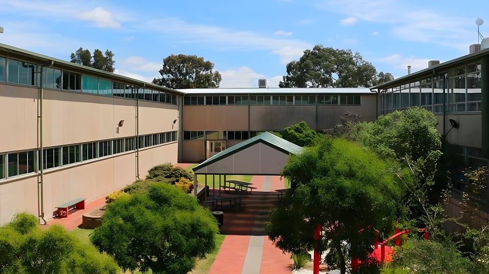 Das mehrstöckige Gebäude mit Innenhof von Modbury High School ist von Bäumen und Sträuchern umgeben.