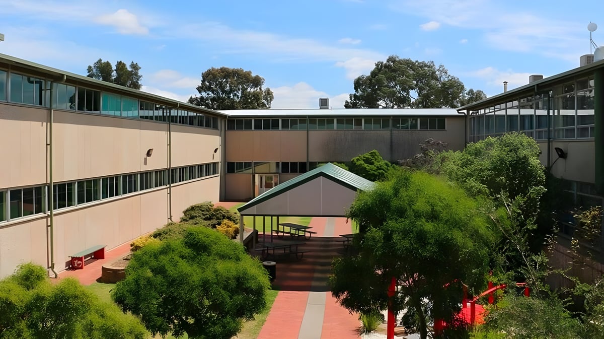 Das mehrstöckige Gebäude mit Innenhof von Modbury High School ist von Bäumen und Sträuchern umgeben.