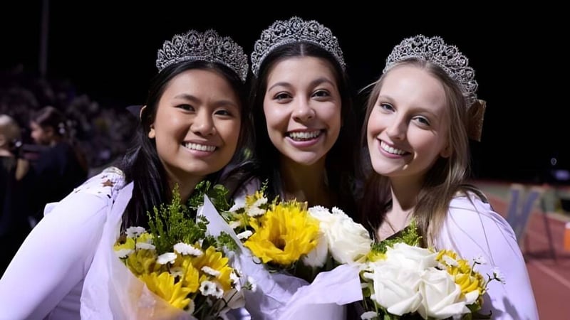 Drei Schülerinnen der Monarch High School tragen verzierte Tiaren und halten gelbe und weiße Blumenbouquets.
