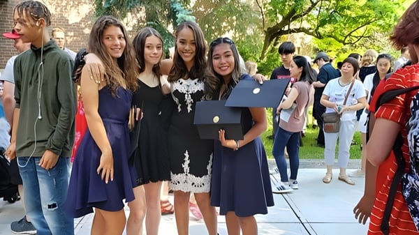 Eine Gruppe junger Absolventinnen steht mit Diplomen im Freien auf dem Campus des Monarch Park Collegiate Institute.