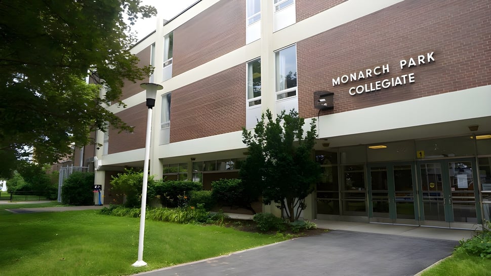 Das Backsteingebäude des Monarch Park Collegiate Institute ist von Bäumen und einer Wiese umgeben.