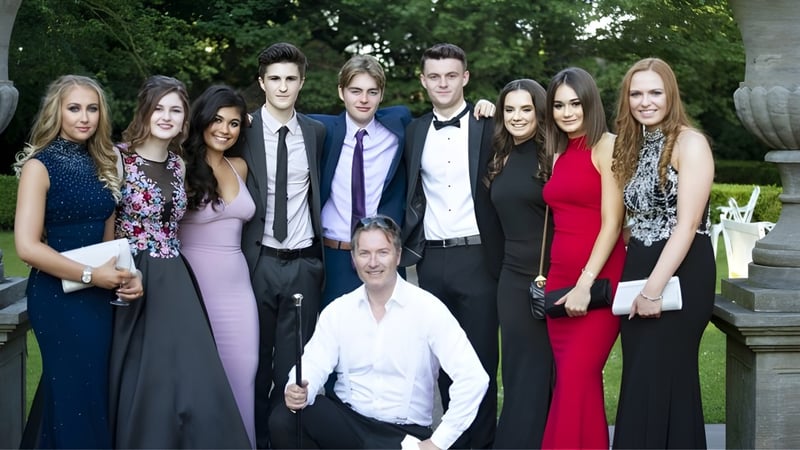 Eine Gruppe gut gekleideter Personen steht zusammen vor grünem Hintergrund auf dem Gelände der Monkton Combe School.