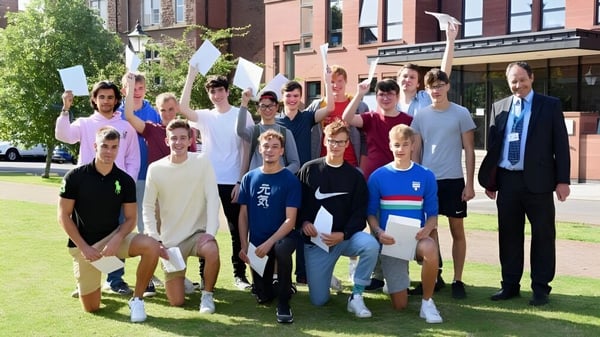 Schüler und Erwachsene stehen gemeinsam auf einer Wiese vor dem Backsteingebäude der Monmouth School for Boys.