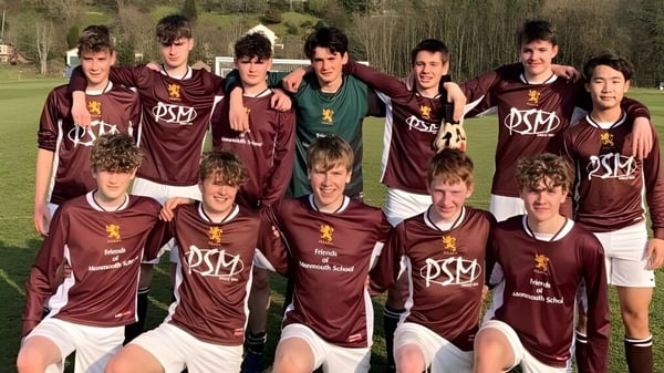 Eine Gruppe von Schülern der Monmouth School for Boys posiert im Sportdress auf einem Rasenfeld umgeben von Bäumen.