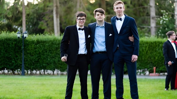 Drei Schüler der Monmouth School for Boys stehen in formeller Kleidung auf einer Wiese vor Bäumen.
