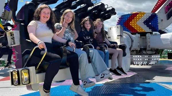 Schülerinnen der Monmouth School for Girls sitzen gemeinsam auf einer Fahrt in einem Freizeitpark mit bunten Karnevalsattraktionen im Hintergrund.
