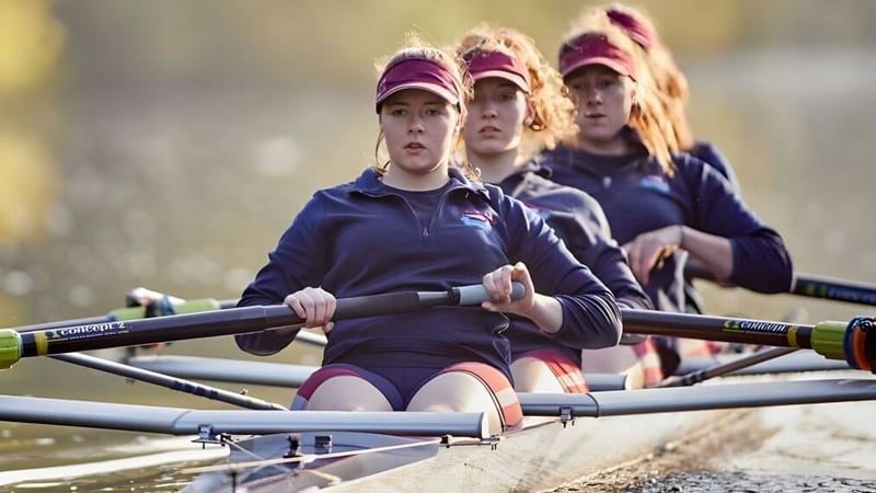 Eine Gruppe von Schülerinnen der Monmouth School for Girls rudert gemeinsam auf dem Wasser vor einer naturnahen Landschaft.