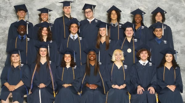 Eine Gruppe von Absolventen der Monsignor Donovan Catholic High School steht gemeinsam in akademischen Gewändern vor einem grauen Hintergrund.