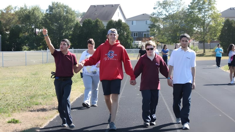Eine Gruppe Schülerinnen und Schüler der Monsignor Doyle Catholic Secondary School geht gemeinsam auf einem gepflasterten Weg zwischen Bäumen und Gebäuden.