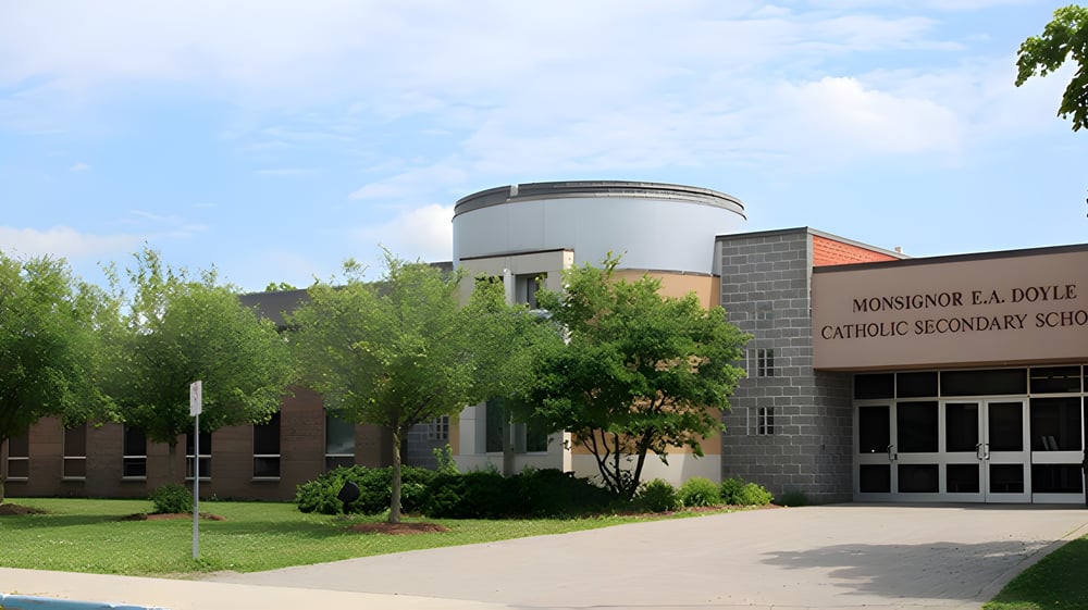 Das moderne Schulgebäude der Monsignor Doyle Catholic Secondary School mit rundem Bauteil steht umgeben von gepflegtem Rasen und grüner Landschaft.