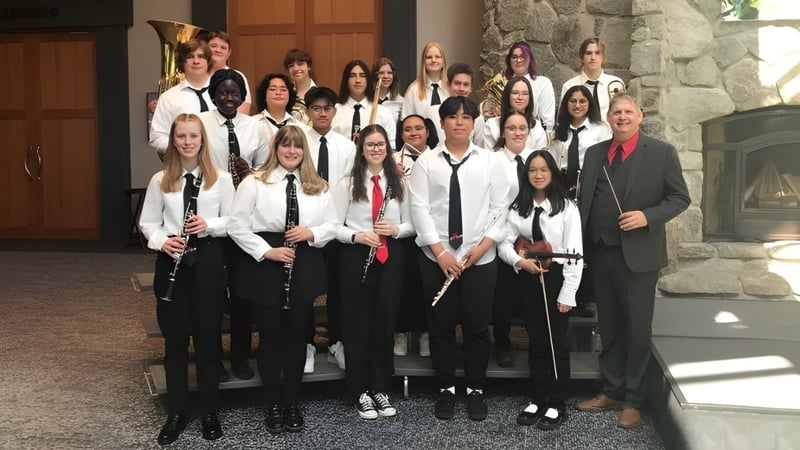 Eine Gruppe von Schülerinnen und Schülern der Monsignor McCoy High School posiert gemeinsam vor einer steinernen Wand und Holztüren.