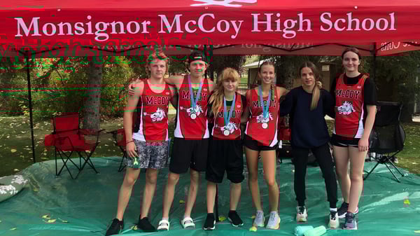 Eine Gruppe von Schülerinnen und Schülern steht vor einem Banner der Monsignor McCoy High School im Freien.