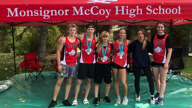 Eine Gruppe von Schülerinnen und Schülern steht vor einem Banner der Monsignor McCoy High School im Freien.