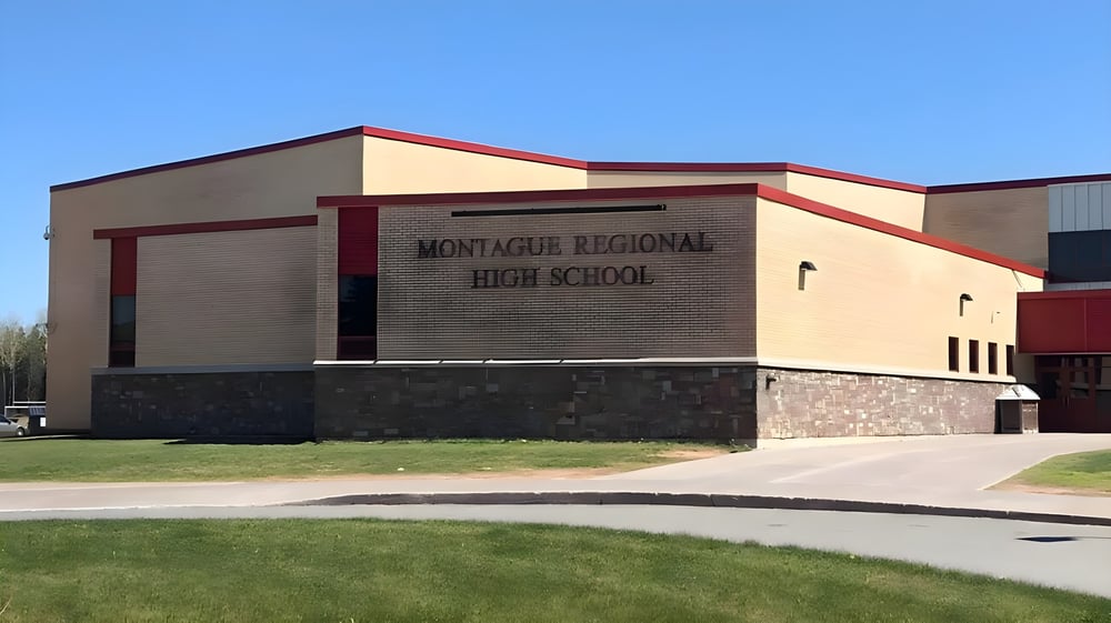 Das moderne mehrstöckige Gebäude mit rotem Ziegeldach der Montague Regional High School steht auf einer Rasenfläche unter klarem Himmel.