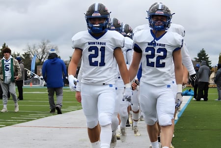 Zwei Footballspieler der Montague Regional High School in weißen Trikots laufen gemeinsam über das Spielfeld.