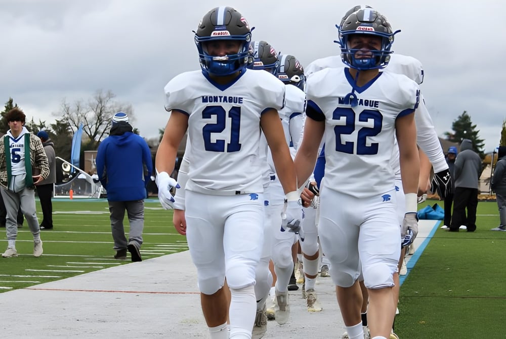 Zwei Footballspieler der Montague Regional High School in weißen Trikots laufen gemeinsam über das Spielfeld.