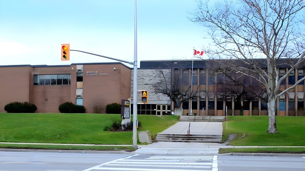 Das Backsteingebäude der Montcalm Secondary School mit einer kanadischen Flagge vorne und Bäumen im Hintergrund.