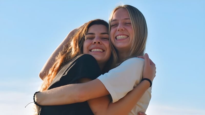 Zwei Schülerinnen umarmen sich vor klarem Himmel auf dem Gelände der Monterey Bay Academy.