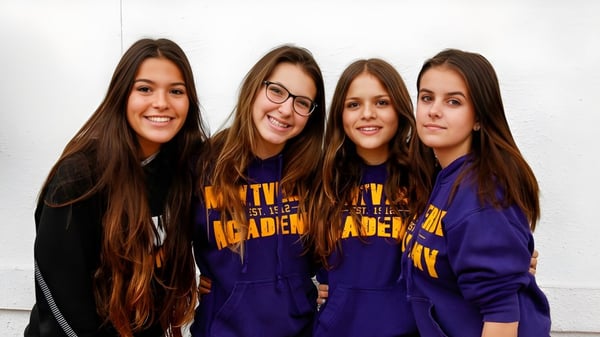 Vier Schülerinnen der Montverde Academy posieren lachend vor weißer Wand in einheitlichen violetten Sweatshirts.