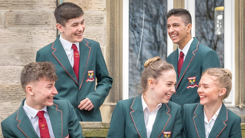 Eine Gruppe von Schülern in Schuluniformen steht vor einem Backsteingebäude auf dem Gelände der Moorland School und unterhält sich.