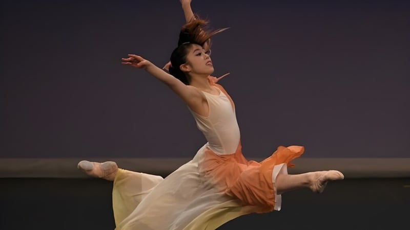 Eine Tänzerin führt auf der Bühne der Moorland School einen Tanz in einem weißen Kleid mit orangen Akzenten auf.