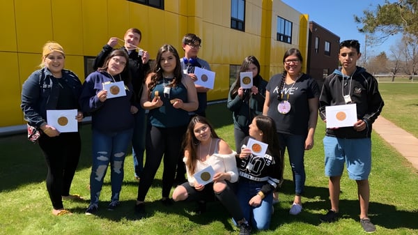 Eine Gruppe von Schülern der Morell Regional High School steht mit Schildern vor einem farbigen Gebäude auf einer Wiese.