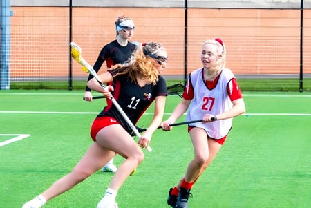 Schülerinnen von Moreton Hall School spielen ein Hockeyspiel auf dem Kunstrasenfeld vor einem Backsteingebäude.