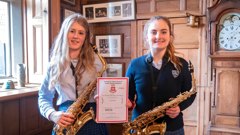 Zwei Schuellerinnen der Moreton Hall School stehen mit Saxophonen in einem Raum mit Holzvertäfelung und antiker Uhr an der Wand.