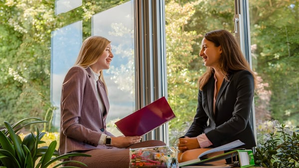 Zwei Schülerinnen der Moreton Hall School stehen vor einem großen Fenster und führen ein Gespräch mit Blick auf eine grüne Umgebung.