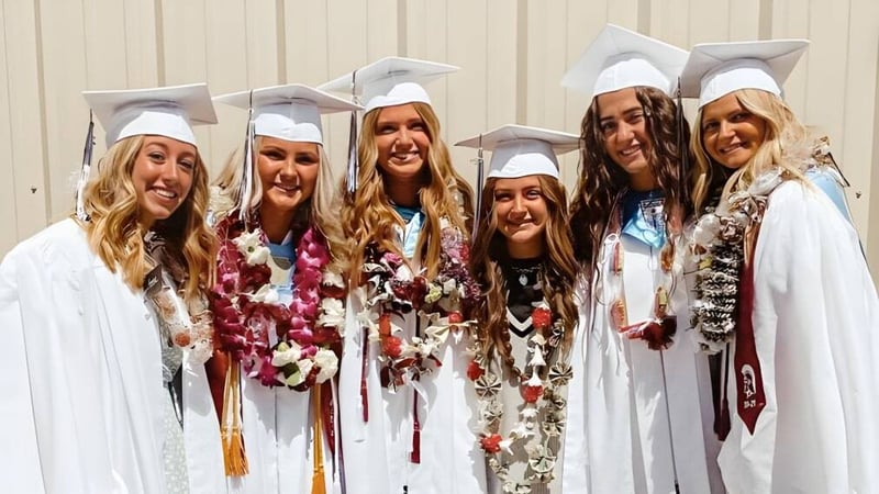 Eine Gruppe junger Absolventinnen der Morgan High School steht in Abschlusskleidung vor einer Holzwand.
