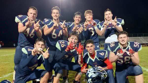 Eine Gruppe von Schülern der Morgan High School posiert in Fußballuniform auf dem Spielfeld bei Nacht unter Flutlicht.
