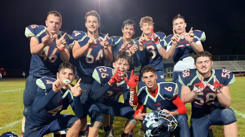 Eine Gruppe von Schülern der Morgan High School posiert in Fußballuniform auf dem Spielfeld bei Nacht unter Flutlicht.