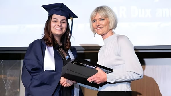 Eine junge Frau in Talar steht mit einer älteren Frau zusammen und hält ein Diplom auf dem Campus der Morley Senior High School.